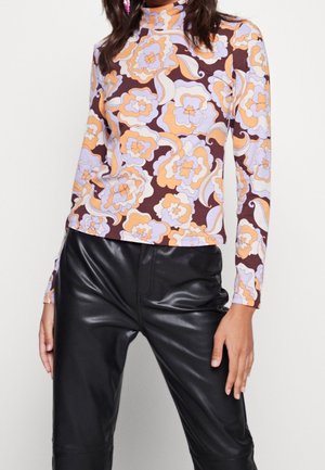 Langärmeliges Rollkragenoberteil mit einem Retro-Blumenmuster in Orange, Lila und Braun auf einem elastischen Stoff; ergänzt durch schwarze Lederhose.