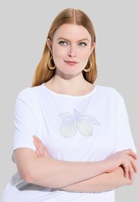 Bílé tričko s krátkým rukávem s designem citronu se žlutými a stříbrnými tečkami uprostřed. Hladká látka s klasickým kulatým výstřihem.