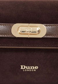 Dark brown suede handbag featuring a glossy brown leather strap and a gold-tone clasp with embossed logo details. "Dune London" logo displayed.