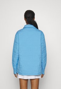 Svetle modrá prošívaná bunda s límcem, zdobená texturovanými geometrickými vzory a dlouhými rukávy. Hladký povrch látky.