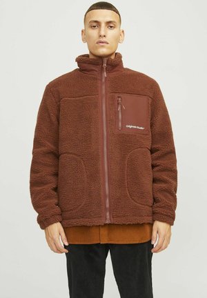 Veste en polaire marron avec un col montant, fermeture éclair et poches avant. Elle possède une poche poitrine contrastante avec fermeture éclair et un détail de logo.