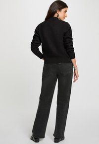 Suéter negro de punto con puños y dobladillo acanalados, combinado con jeans oscuros de tiro alto en gris. Los jeans presentan un diseño clásico de cinco bolsillos.