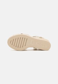Semelle de sandale compensée beige avec grip texturé, trous de ventilation et nom de marque en relief "Geox" visible, photographiée sur fond blanc.