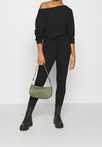 Sudadera negra con los hombros al descubierto y pantalones ajustados a juego, combinados con un bolso en verde oliva y botas negras de combate con cordones.