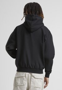 Svart huvtröja med avslappnad passform, elastisk midja och manschetter. Slät tygstruktur med en enkel, minimalistisk design.