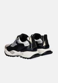 Zapatillas bajas en negro, plateado y dorado con suelas texturizadas en blanco y tiradores negros en el talón, anguladas para mostrar la parte trasera y los lados exteriores.