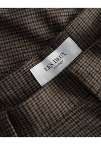 Brown checkered fabric with a subtle texture, featuring a white label printed with "LES DEUX copenhague" integrated into the design.