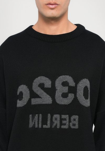 Schwarzer Strickpullover mit einem gerippten Rundhalsausschnitt. Auf der Vorderseite prangt in großen grauen Buchstaben der Schriftzug "032 BERLIN".