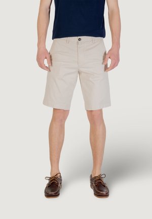 Shorts beige avec une coupe droite, dotés d'une fermeture à bouton, de passants de ceinture et de poches latérales, associés à des chaussures de bateau marron.