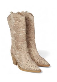 Botas de vaquero beige desnudas con una superficie de tela texturizada y ondulada, punta afilada y tacón apilado. Dos lengüetas en la parte superior.