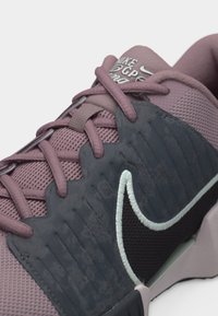 Κοντινή λήψη ενός αθλητικού παπουτσιού Nike σε μωβ και σκούρο γκρι χρώμα με λεπτομέρειες στα κορδόνια, υφασμάτινη διαπνέουσα επιφάνεια και κεντημένο λογότυπο swoosh στο πλάι.