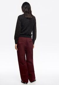 Suéter de punto gris oscuro con mangas abullonadas, combinado con pantalones burdeos de cintura alta que cuentan con bolsillos traseros y un corte ajustado.