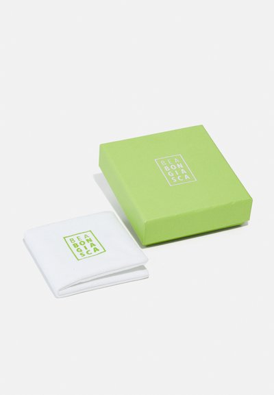 Weißes Stoffstück, gefaltet neben einer grünen Box. Die Box zeigt ein weißes Logo-Design. Das Stück hat ein ähnliches Logo in grüner Stickerei.