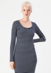 Μπλε ριγέ φόρεμα με μακριά μανίκια, ριγωτή υφή και στρογγυλή λαιμόκοψη. Διαθέτει λευκές οριζόντιες ρίγες και εφαρμοστή γραμμή.