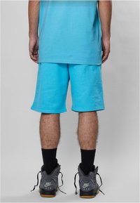 Turkise bomullsshorts med elastisk midje, ribbet kant og avslappet passform, kombinert med grå Nike høye sko og svarte sokker.
