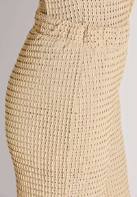 Beige textuurbroek met een golvend patroon met kleine openingen, een glad oppervlak en een nauwsluitend ontwerp met een hoge tailleband.