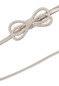 Cintura argentata con una fibbia a fiocco decorata con cristalli, caratterizzata da una banda liscia e una sezione testurizzata. Il colore complessivo è un beige chiaro.