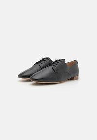 Black leather shoes with a pointed toe and lace-up design. Smooth texture, minimalistic detailing, and a low wooden heel.