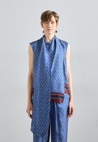 Siniste kangast ilma varrukateta top, millel on geomeetriline muster, drapeeritud sall, marooni aktsendid ja sile, läikiv tekstuur.