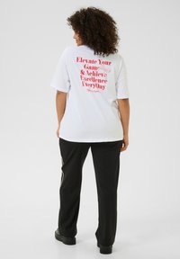 T-shirt blanc à manches courtes avec un texte rose vif au dos. Assorti à un pantalon noir. Matériau en coton doux.