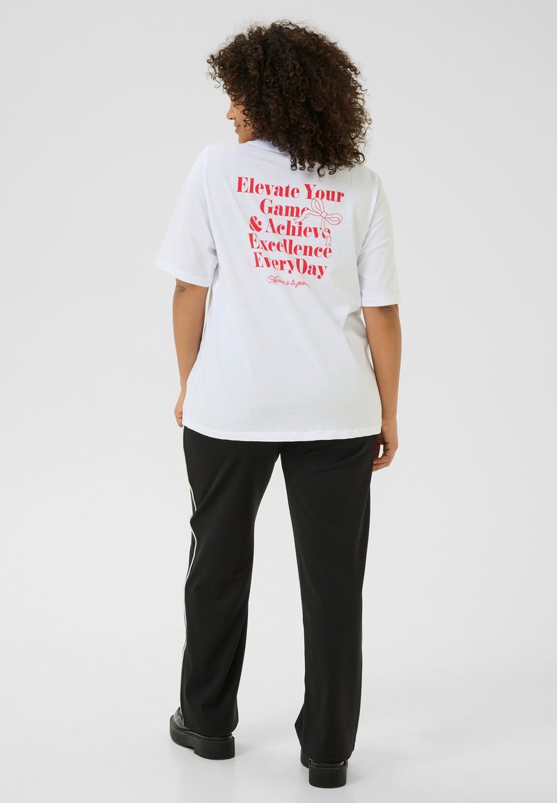 T-shirt blanc à manches courtes avec un texte rose vif au dos. Assorti à un pantalon noir. Matériau en coton doux.