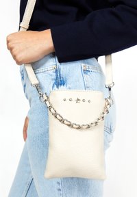 Kremowa torebka crossbody z materiału skóropodobnego z srebrnym łańcuszkiem, ozdobiona dekoracyjnymi ćwiekami i akcentem w kształcie gwiazdy z przodu.