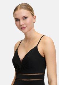 Zwarte jurk met dunne bandjes, met een diepe halslijn, geplooide details en een doorzichtige meshaccent bij de taille. Gladde stoftextuur.