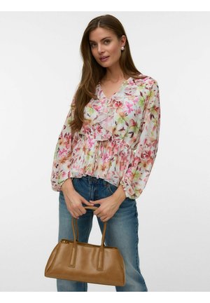 Hosszú hajú nő virágmintás fodros blúzban és kék farmerral, barna bőrtáskát tart mindkét kezével.