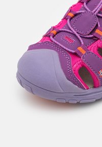 Shoe desportivo em tons de roxo e rosa com sola de borracha texturizada, biqueira reforçada e atacadores ajustáveis. Aberturas laterais para ventilação.