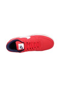Zapatilla textil roja con un swoosh blanco de Nike. Presenta cordones rojos, un interior azul marino y una suela de goma beige. Marca impresa en la lengüeta.