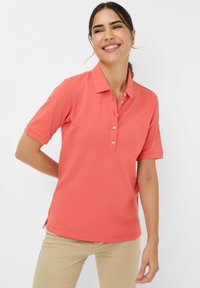 Polo shirt corallo con maniche corte, colletto classico, apertura a tre bottoni, spacchi laterali, realizzato in tessuto morbido e leggero.