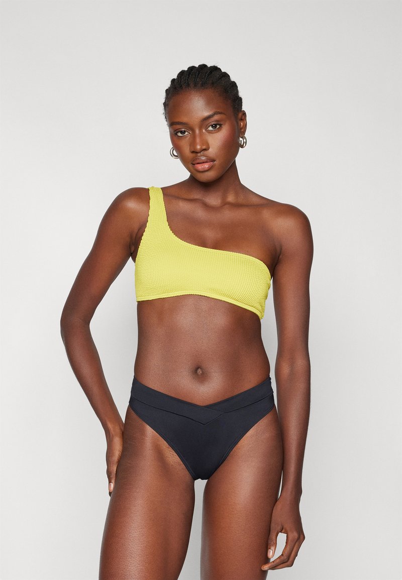 Gul en-skulder bikini topp med ribbet tekstur, kombinert med høyt liv svarte bikini truser med chevron-kutt.