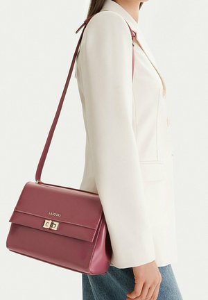 Frau trägt weißen Blazer und blaue Jeans und trägt eine kastanienbraune Lasocki Schultertasche mit goldener Schnalle auf ihrer rechten Seite.