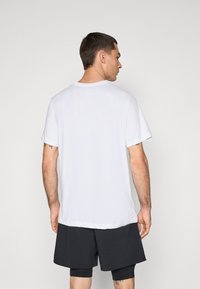 Hvit kortermet t-skjorte med rund hals, myk stoff og avslappet passform, kombinert med mørke shorts, vist fra baksiden.