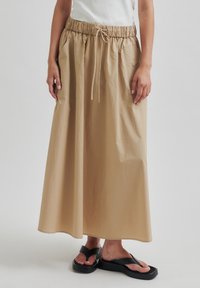 Fustă bej, până la glezne, cu talie elastică și șnur de ajustare. Material neted, ușor, cu o croială lejeră.