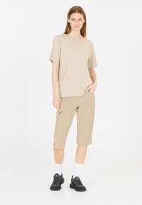 Beige t-shirt med kort ärm och knälånga beiga shorts, kombinerat med svarta träningsskor och vita strumpor. Shortsen har en sidofick.