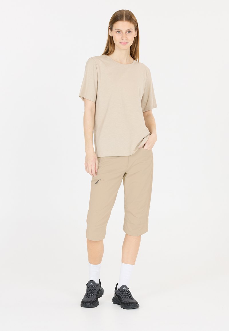 Beige t-shirt med kort ärm och knälånga beiga shorts, kombinerat med svarta träningsskor och vita strumpor. Shortsen har en sidofick.