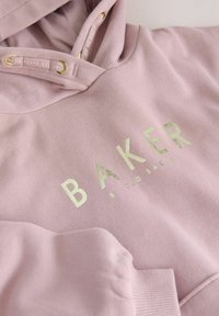Light pink hoodie with a soft texture. Features a gold foil "BAKER" logo and gold accents in the drawstring eyelets.