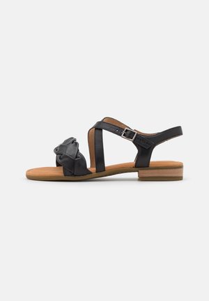 Sort flad sandal med snoet frontrem, ankelrem med sølvspænde, polstret tan-farvet indersål og lav træblokken hæl.