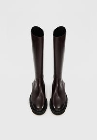 Bottes en cuir marron, montantes, avec une finition lisse, bout rond, semelle noire épaisse et un design sans couture.