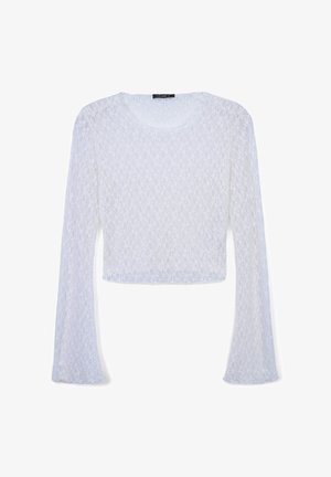 Haut blanc à manches longues en dentelle, avec un col rond et des manches évasées. Le tissu présente un motif délicat et texturé.