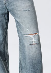 Light blue denim jeans with distressed areas at the knee, featuring frayed edges and visible stitching for texture. Classic straight-leg design.