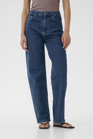 Jeans scuri a vita alta con una linea dritta, stile a cinque tasche e dettagli di cuciture visibili. Abbinati a infradito nere.