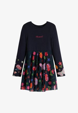 Berete rojo, bufanda larga roja con degradado, marca negra, vestido azul marino con estampado colorido de flores y mariposas, calcetas rojas hasta la rodilla, zuecos beige.