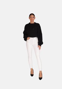 Pull noir en tricot avec un motif en diamant texturé, associé à un jeans blanc ajusté et des escarpins noirs. Design de tenue simple et moderne.