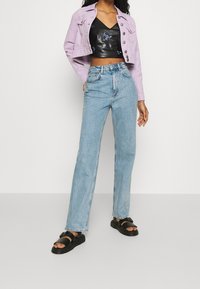 Krótkie dżinsowe kurtki w kolorze lawendy, czarny skórzany top z haftem w kwiaty, niebieskie dżinsy straight leg oraz czarne sandały na paski.