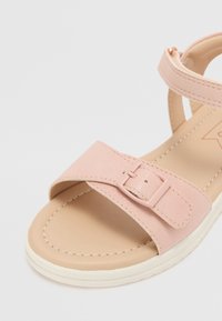 Les sandales roses présentent deux larges brides avec une boucle, une tige lisse semblable au cuir et une semelle texturée avec un bord blanc.