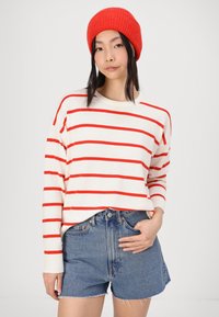 Pulover alb cu dungi roșii orizontale, guler rotund și mâneci lungi, asortat cu şorturi din denim uzat. Căciulă tricotată roșie pe cap.