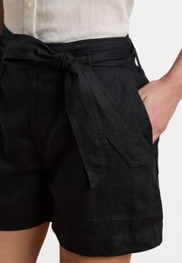 Calções de linho pretos com um cinto de cintura atado, apresentando bolsos laterais e uma textura subtil. Design simples, adequado para climas quentes.
