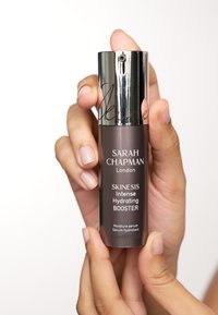 Dunkelbraune Flasche mit einem glänzenden silbernen Pumpenkopf. Das Etikett lautet "SARAH CHAPMAN London SKINESIS Intense Hydrating BOOSTER," 30ml.